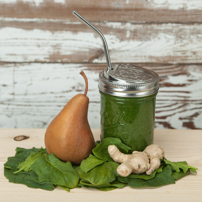 Wide mouth mason jar with a stainless steel drink lid on top with a stainless steel bent straw, filled with a green smoothie.