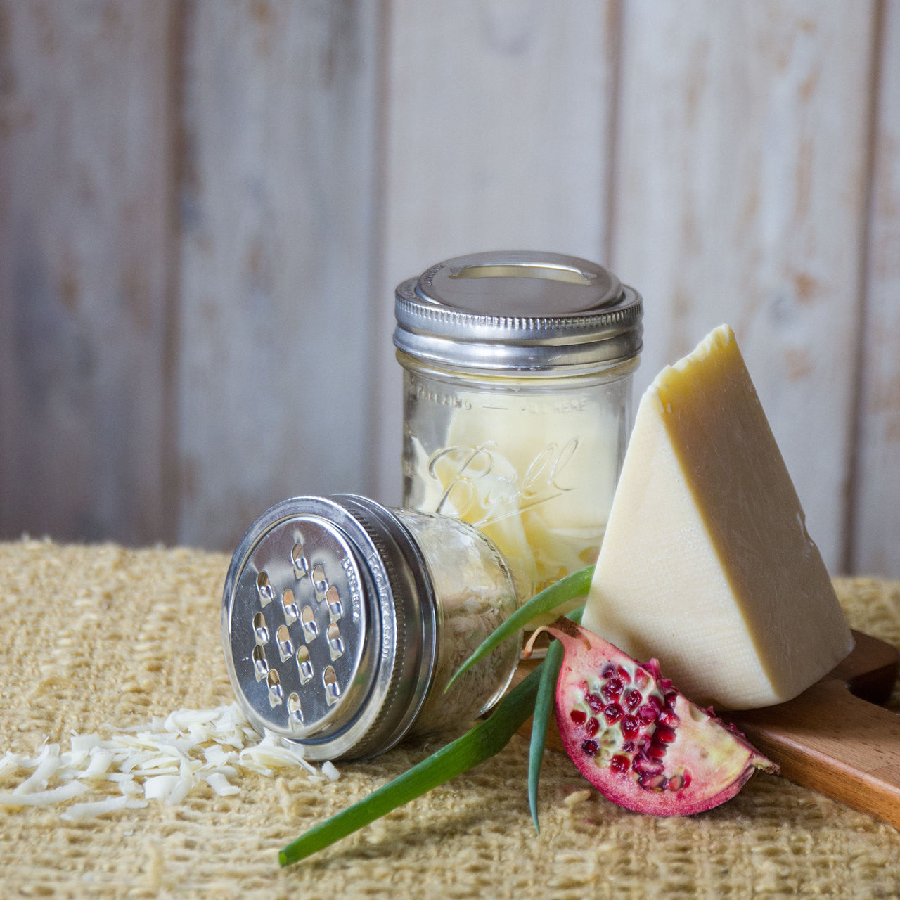 one mason jar with a grater lid and one mason jar with a slicer lid and a wedge of cheese