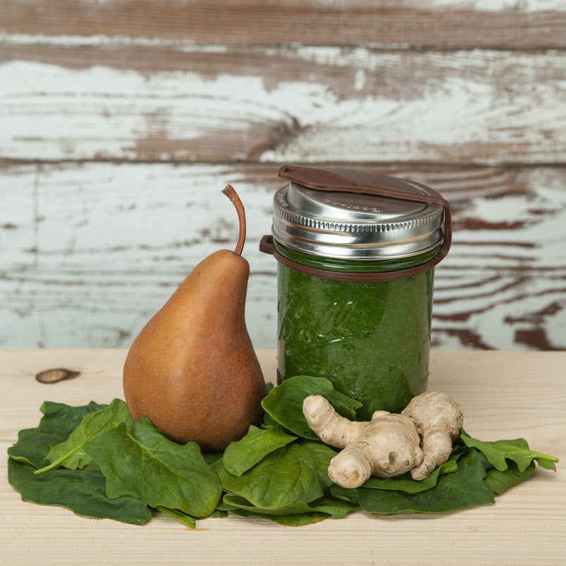 A wide mouth mason jar with a poptop lid closed with a silicone plug, filled with a green smoothie.