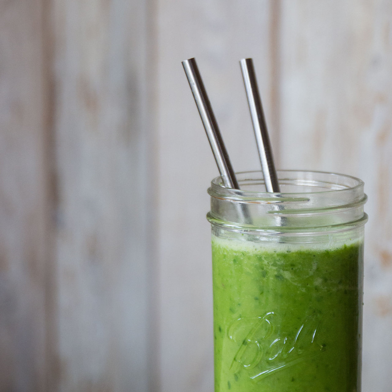 Two smoothie straws in a 32 ounce mason jar filled with a green smoothie.
