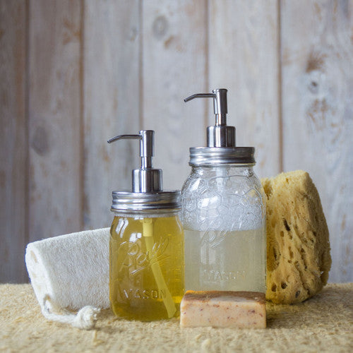 two stainless steel soap pumps on two regular mouth mason jars full of liquid soap, next to sponges